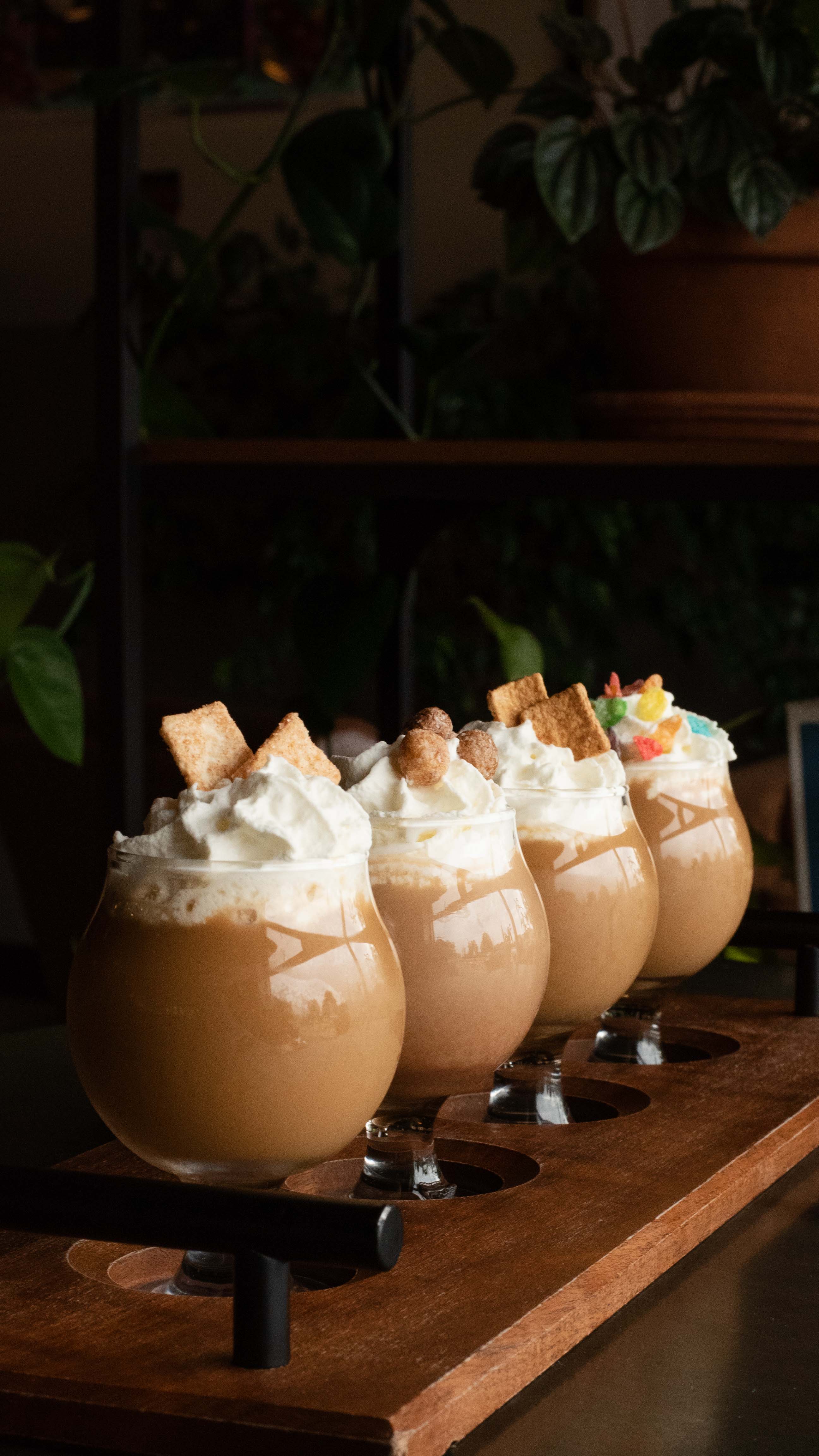 Four 5oz belgian glasses filled with cereal milk flavored cold brew coffees, each topped with whipped cream, and a cereal garnish